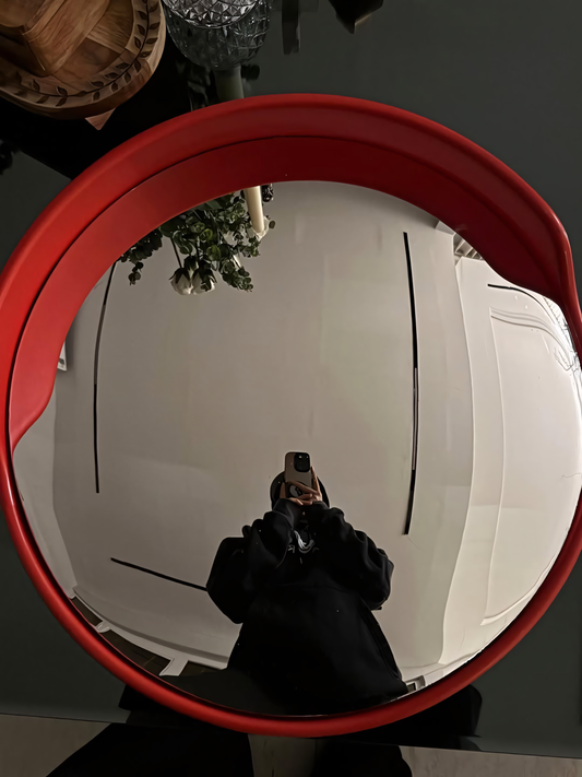 Person taking a mirror selfie with a red frame, reflecting a room interior.